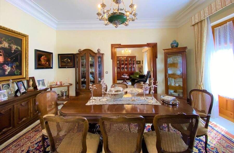 The office, with a long dining table and chairs, two glazed display cabinets, and a wide opening through to the library beyond.