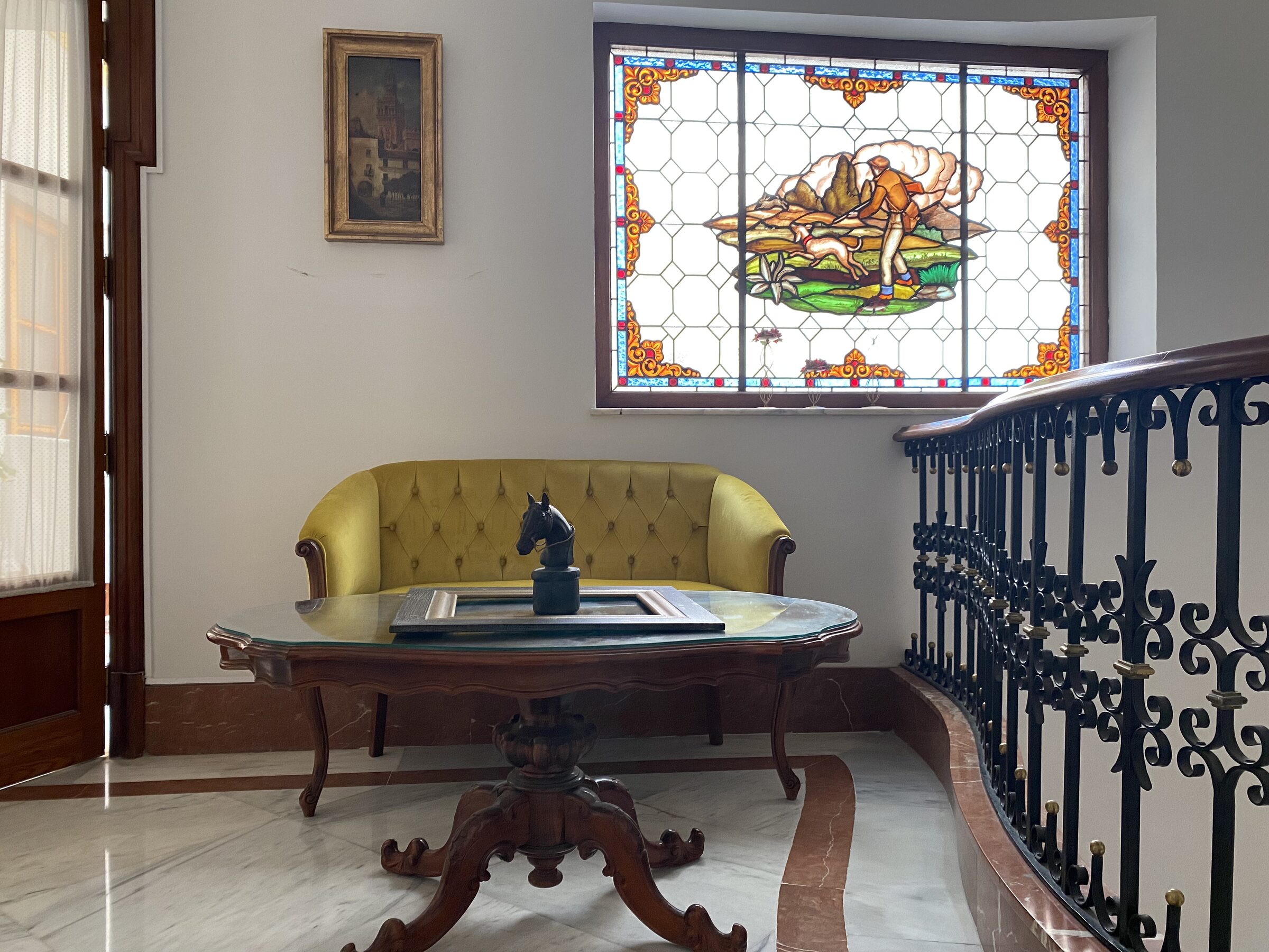 A figurative leaded stained-glass window with a country scene, set above a wrought-iron landing rail.