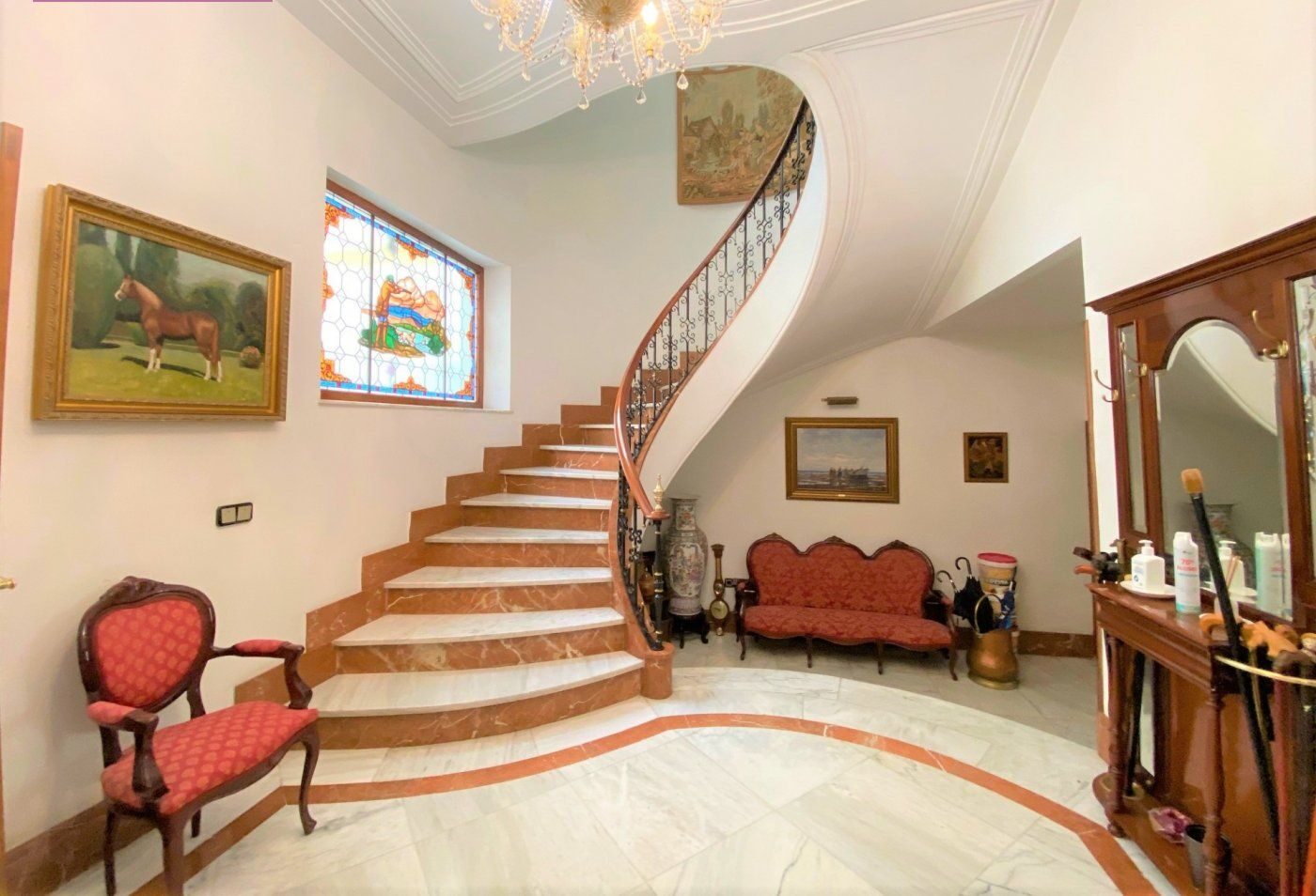 The imperial curved staircase rising under a large crystal chandelier, leaded glass and mahogany handrail.